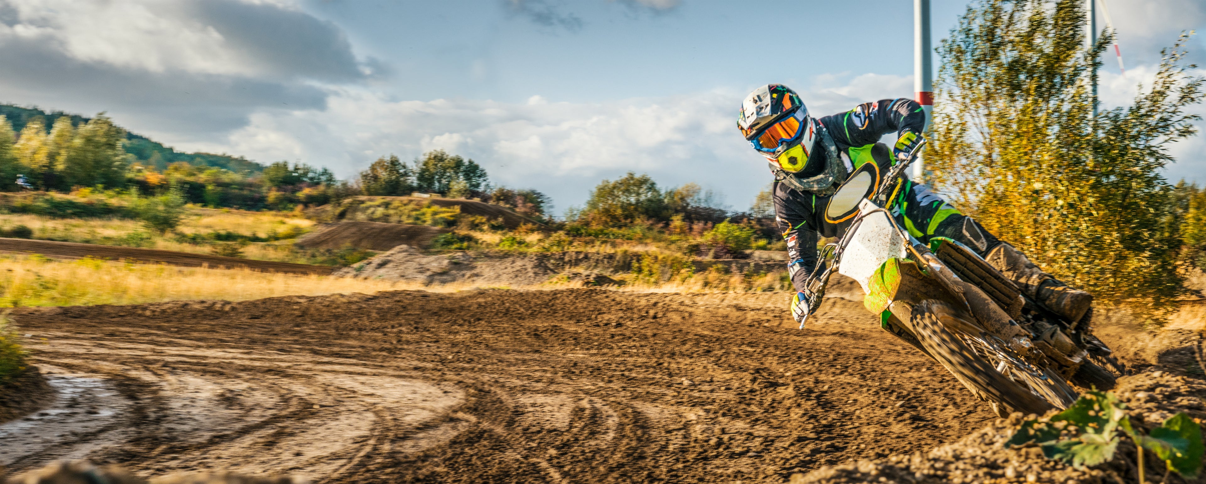 Motocross rider in action on a dirt track with trees and sky in the background